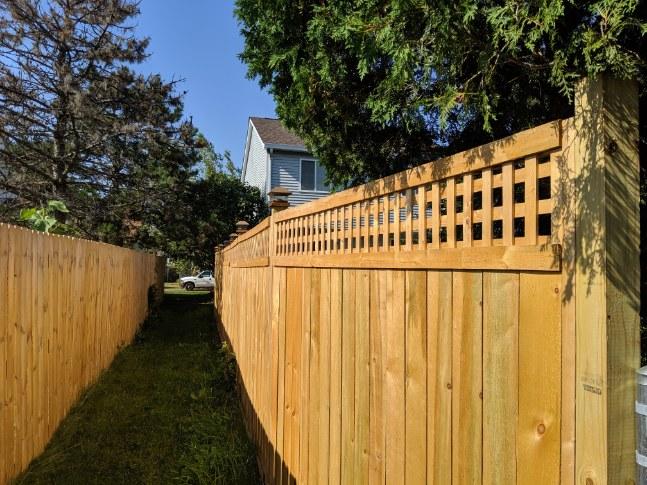 A picture of a alternating panel fence that meets up to a flat wooden fence.